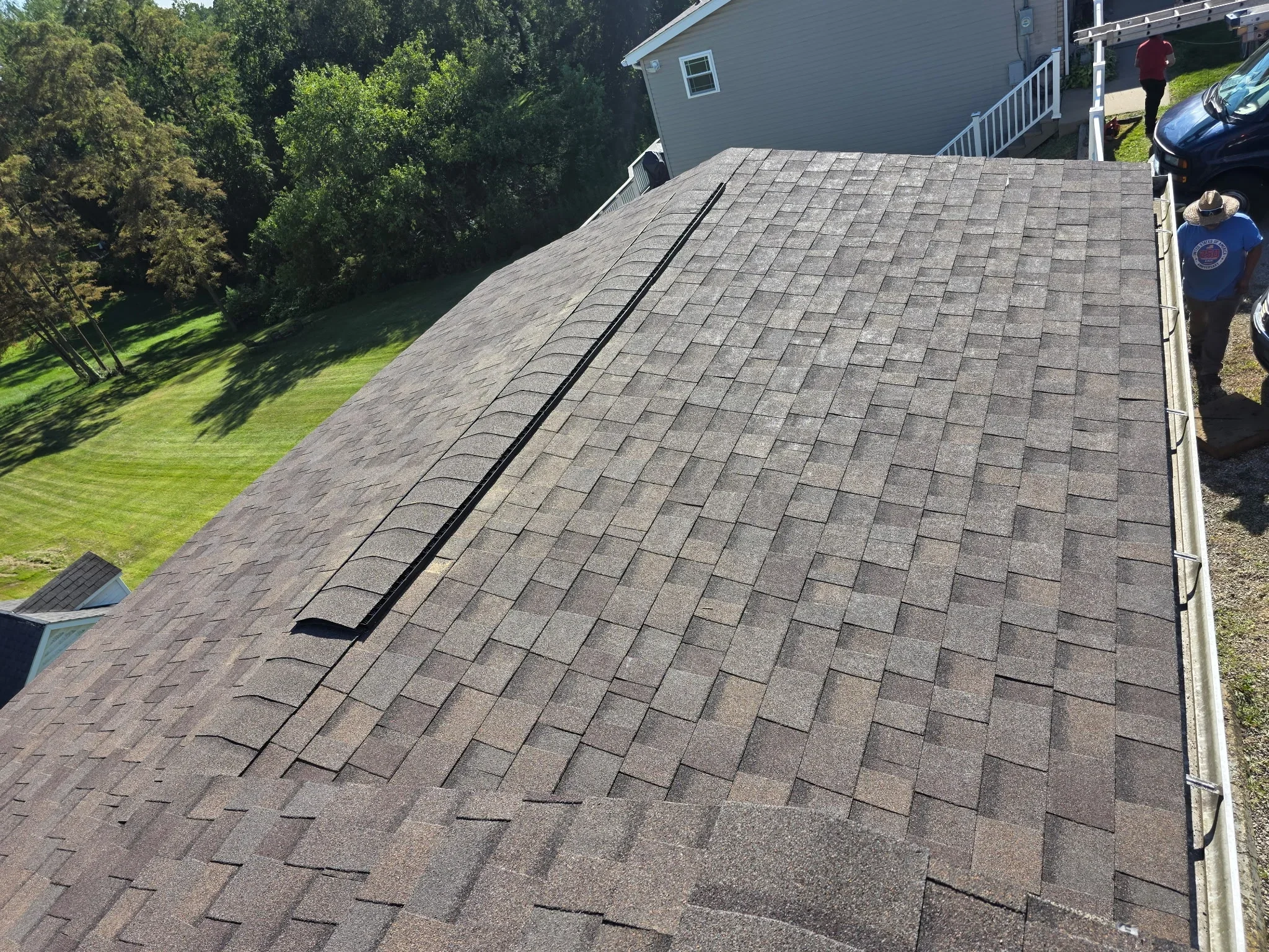 Gray architectural shingles installed on sloped roof with ridge vent and white gutters