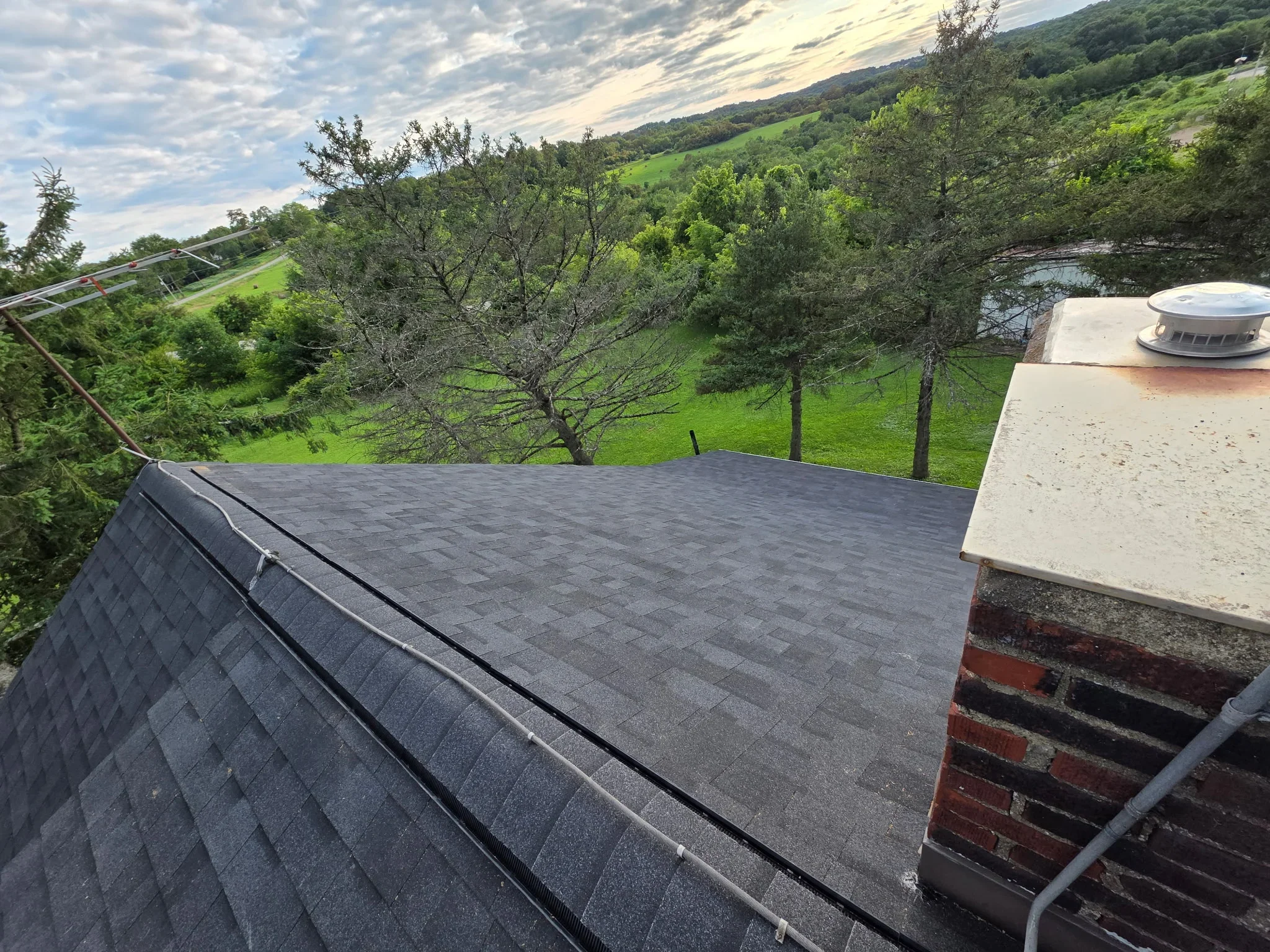 Dark gray asphalt shingles installed on pitched roof with metal flashing and brick chimney