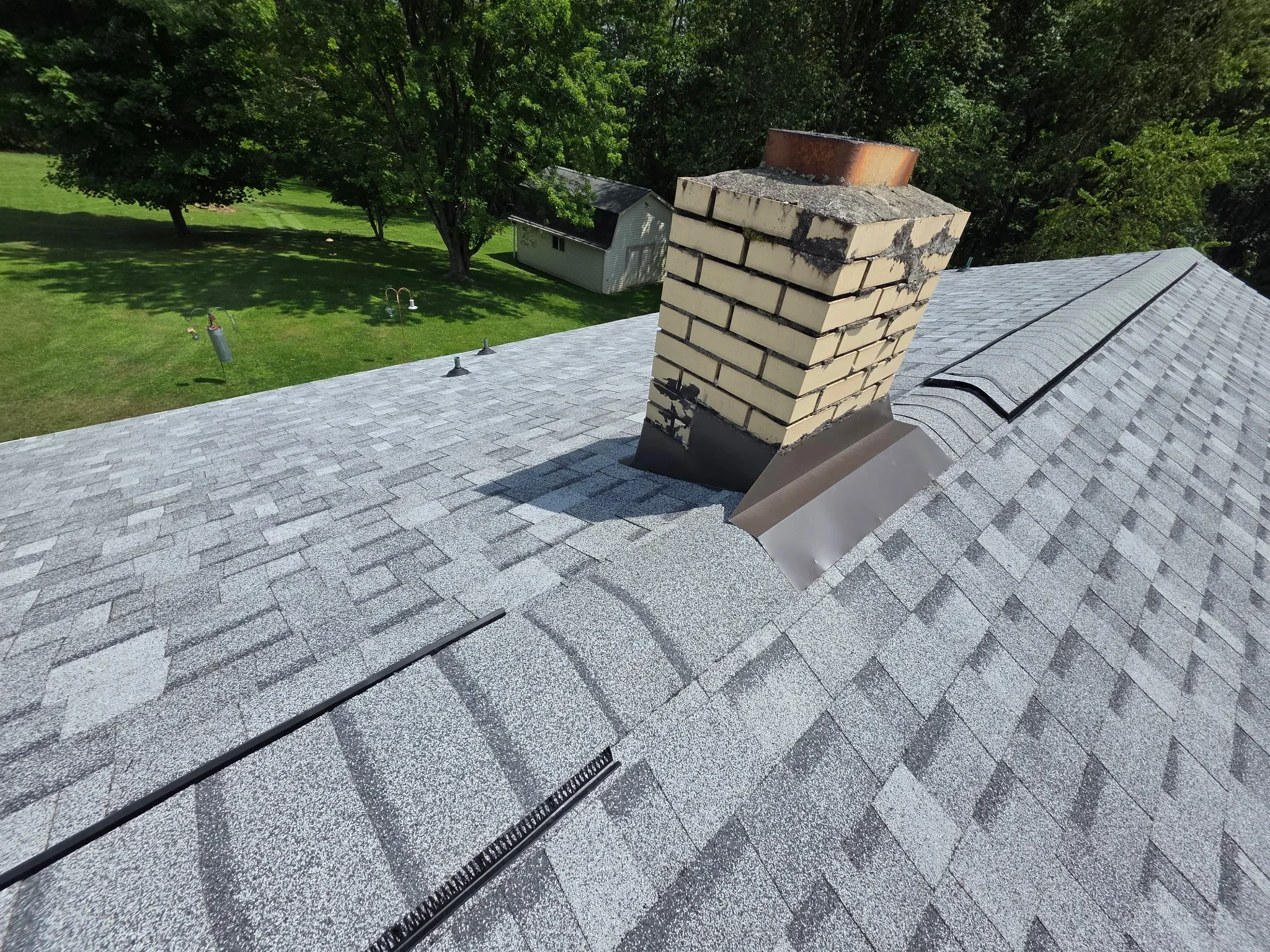 Gray architectural shingles with brick chimney, metal flashing, and drip edge on residential roof