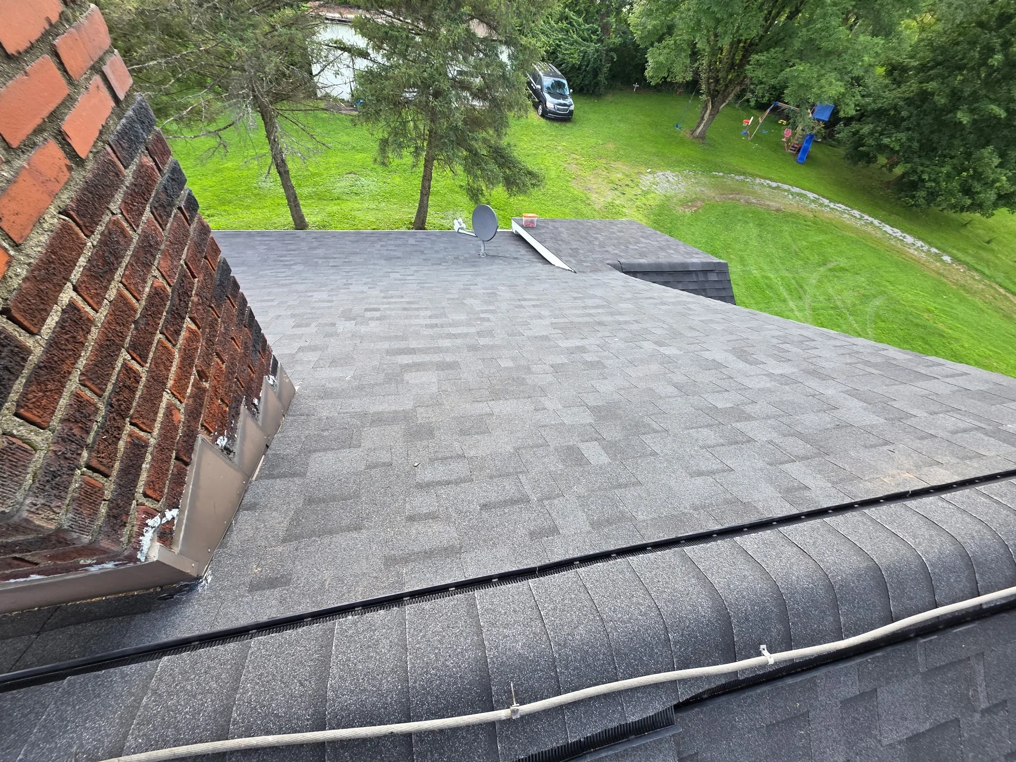 Dark gray asphalt shingle flat roof installation with brick chimney flashing and edge trim
