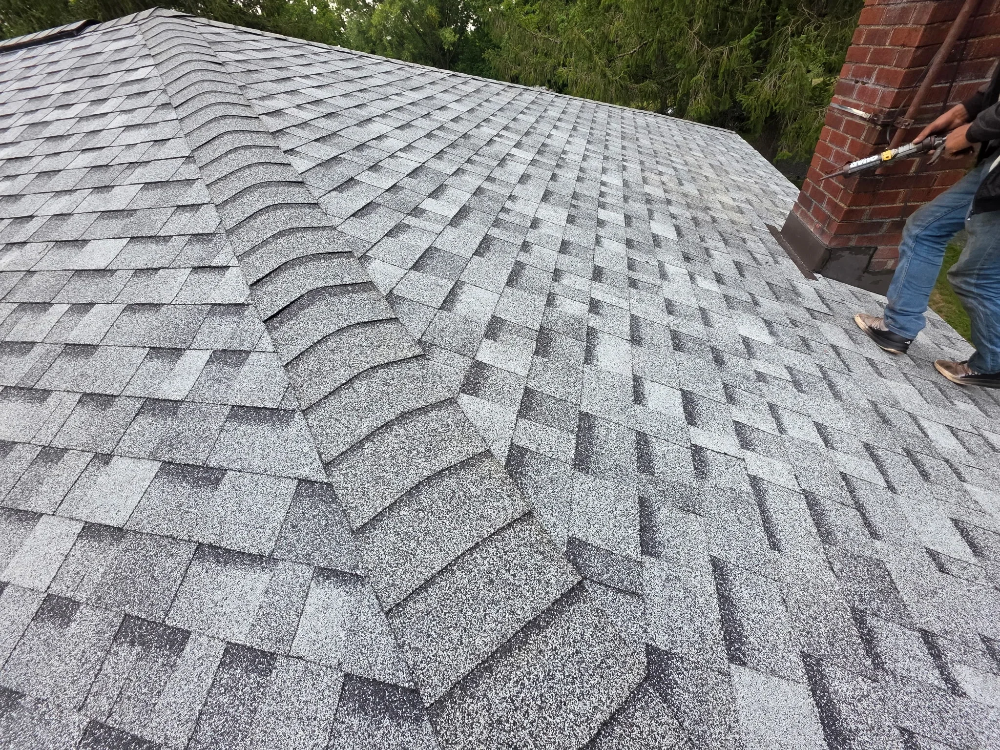 Gray architectural asphalt shingles installed on residential roof with brick chimney visible