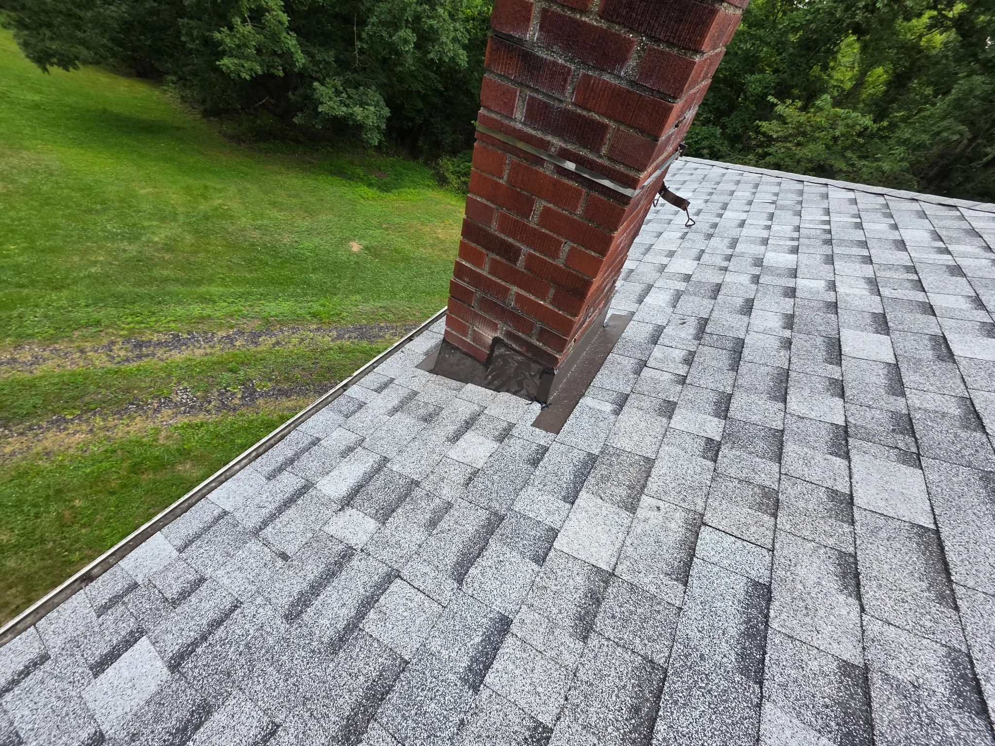 Gray architectural shingles installed on sloped roof with brick chimney flashing