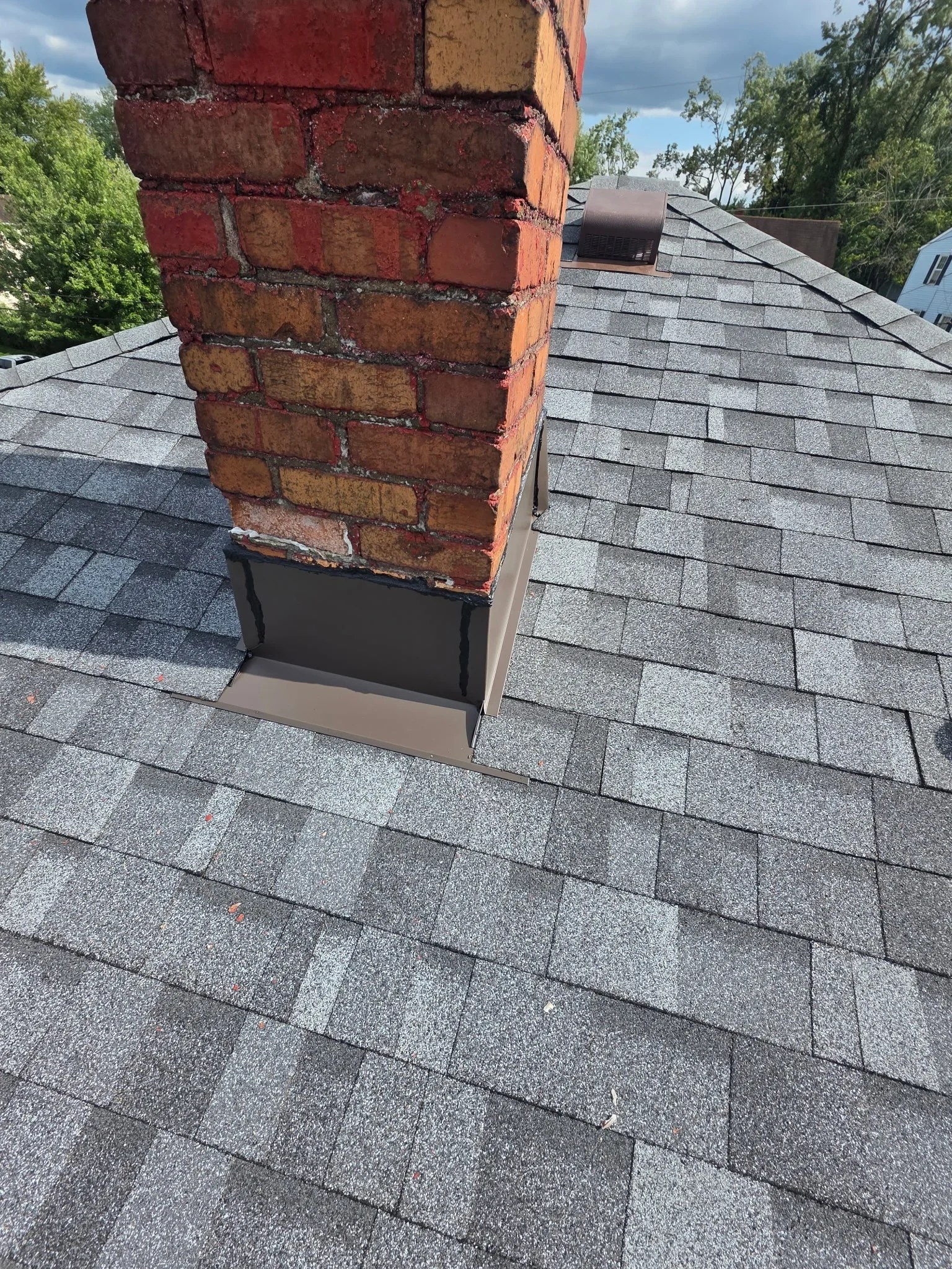 Gray asphalt shingles with brick chimney flashing and black trim on residential roof