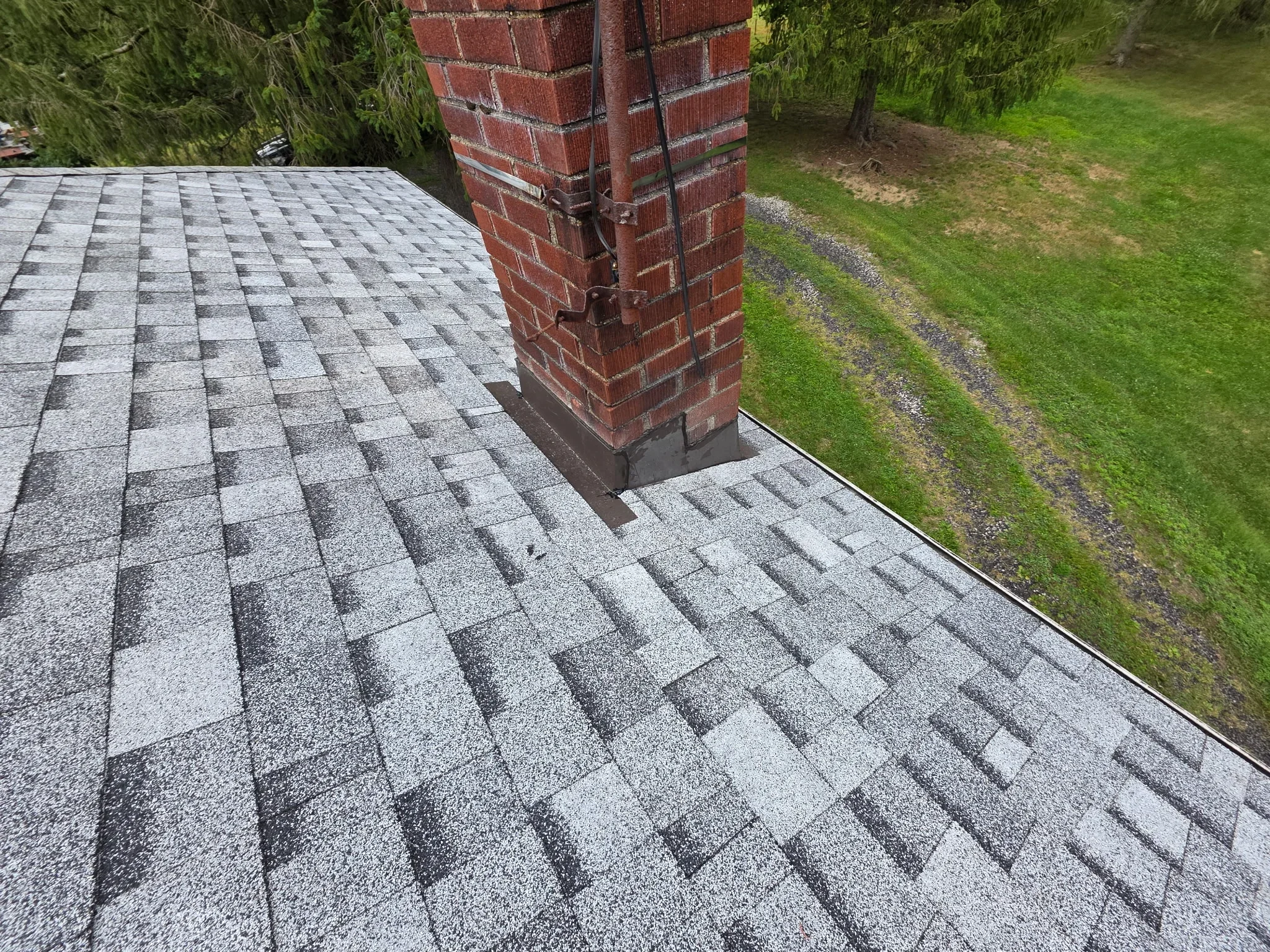 Gray architectural shingles installed on roof with brick chimney flashing and metal drip edge
